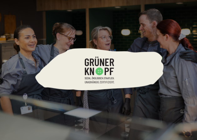 Ein Küchenteam, davor ist das Logo von "Grüner Knopf" zu sehen.