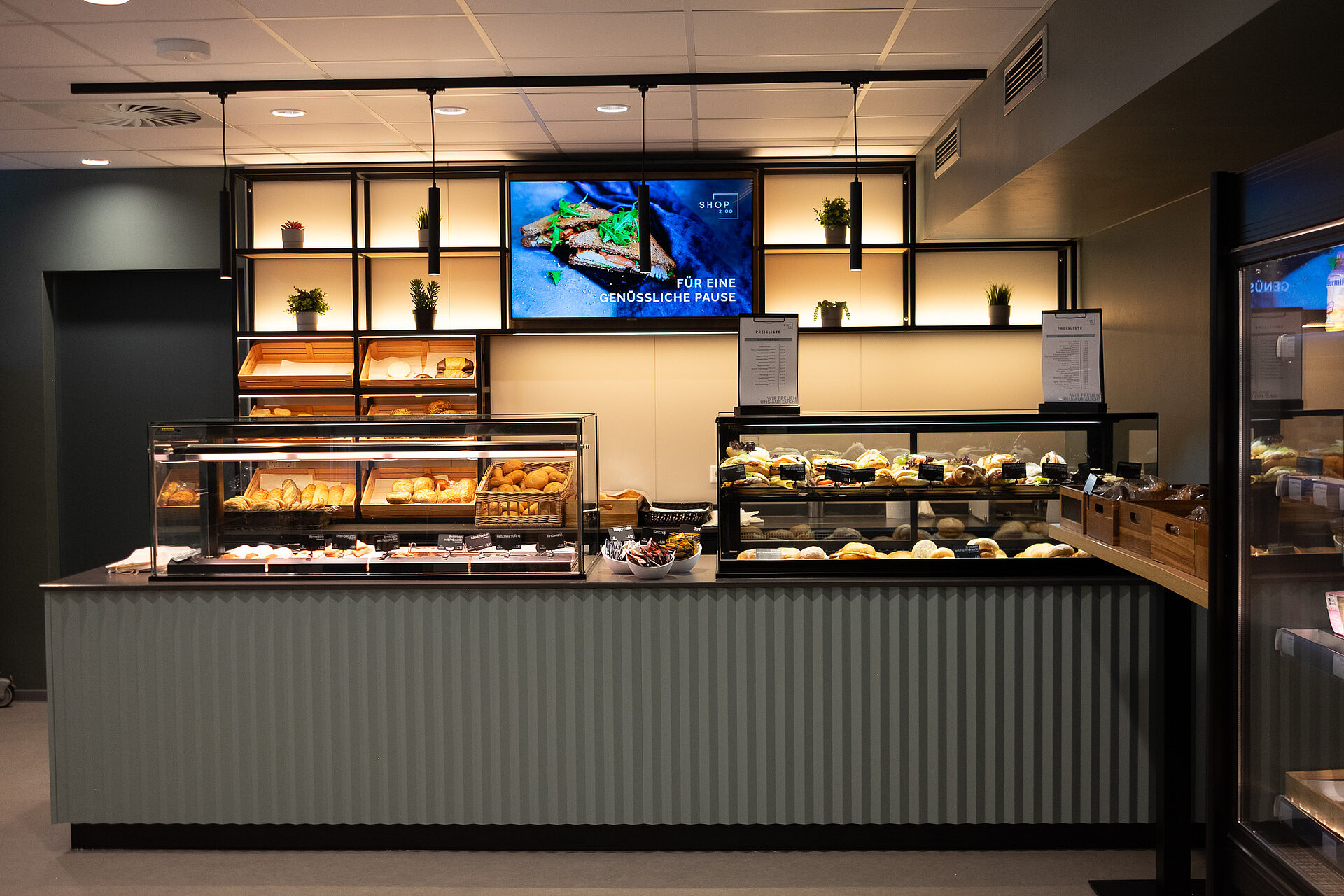 Eine Theke/Kaffeebar, die schön gestaltet und beleuchtet ist. Mittig ist ein Monitor mit einer Stulle platziert.