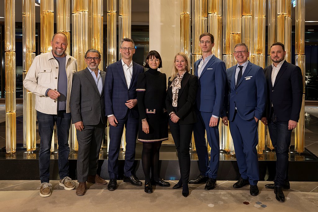 Ein Bild von Manager:innen in Businesskleidung - Anzügen und Kostümen - sie stehen in einer Lobby.