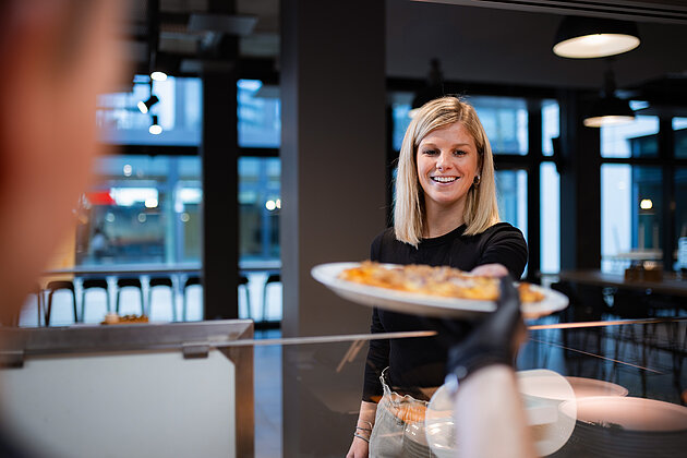 Kunden- & Gastfokussierung Eine junge blonde Dame, die ein Gericht entgegennimmt. Es ist eine Pizza.