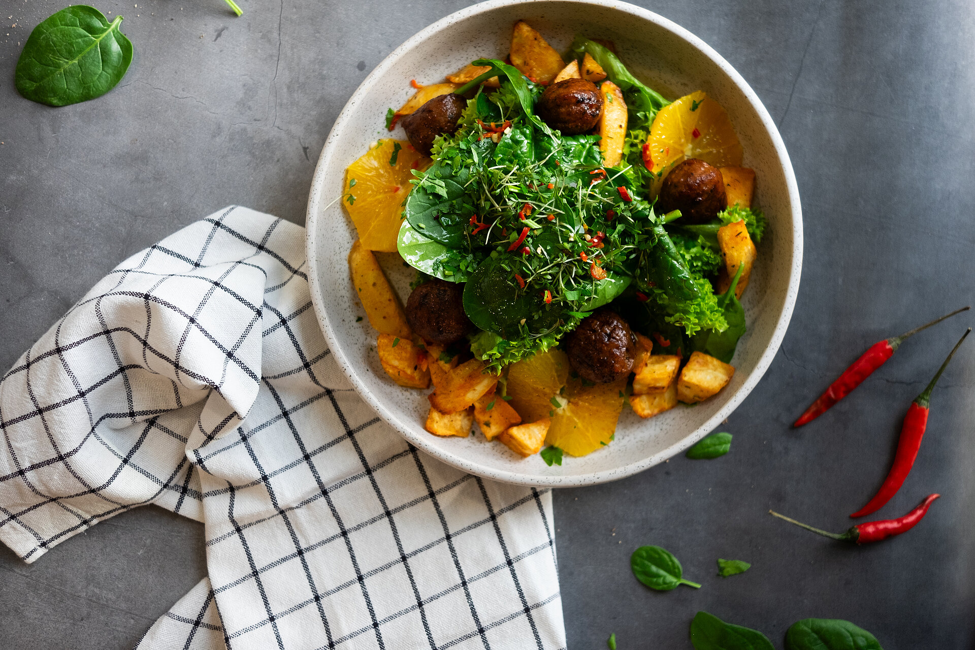 Ein Bild von einem veganen Gericht. Es dürften Süßkartoffeln sein, mit Blattspinat und Petersilie als Topping. Daneben liegen Chilischoten und das Gericht ist schön inszeniert.