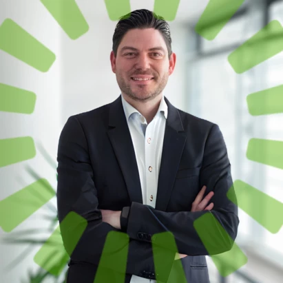 Ein Mann, der seine beiden Hände verschränkt hat und freundlich in die Kamera lächelt. Das Bild stellt ein Business Portrait dar.