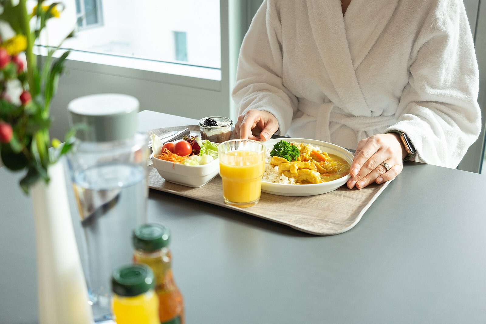 Eine Patientin im Krankenhaus, die an einem Tisch sitzt und ihr Essen auf dem Tablet vor sich hat. Die Mahlzeit sieht sehr gesund aus. 