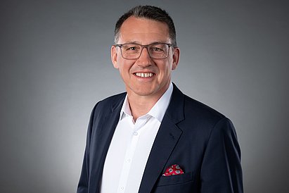 Ein Mann in Hemd und Sakko der freundlich in die Kamera lächelt.