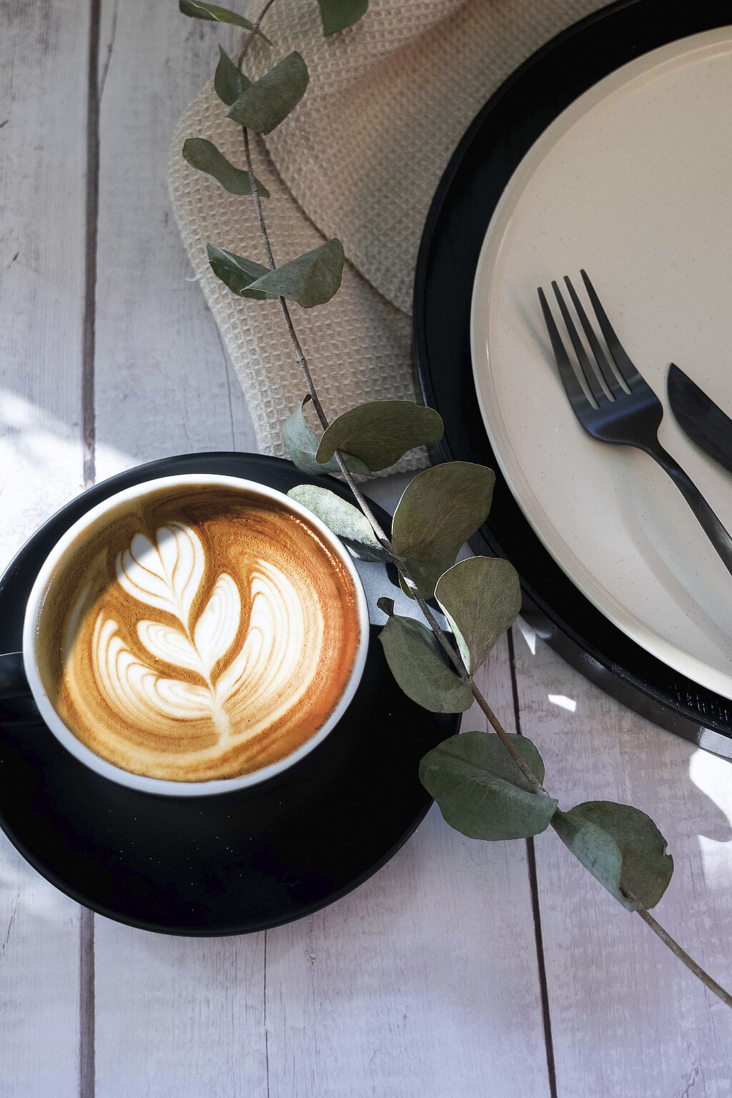 Ein Cappuccino in einer schwarzen Tasse. Im Milchschaum wurde mit Latteart ein Herz reingemalt.