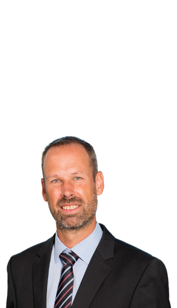 Ein Mann im Sakko und Business Kontext, der freundlich in die Kamera lächelt.