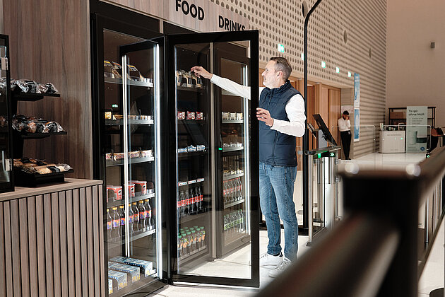 Shop2Go Ein Mann der die Kühlschranktür von einem Shop2Go geöffnet hat und sich am Sortiment bedient.