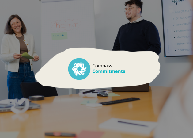Compass Commitments Eine junge Dame und ein junger Mann, die neben einem Flipchart stehen auf dem das Wort Respekt steht. Darüber ist das Logo der Compass Commitments "Respekt, Wachstum, Teamarbeit" zu sehen.