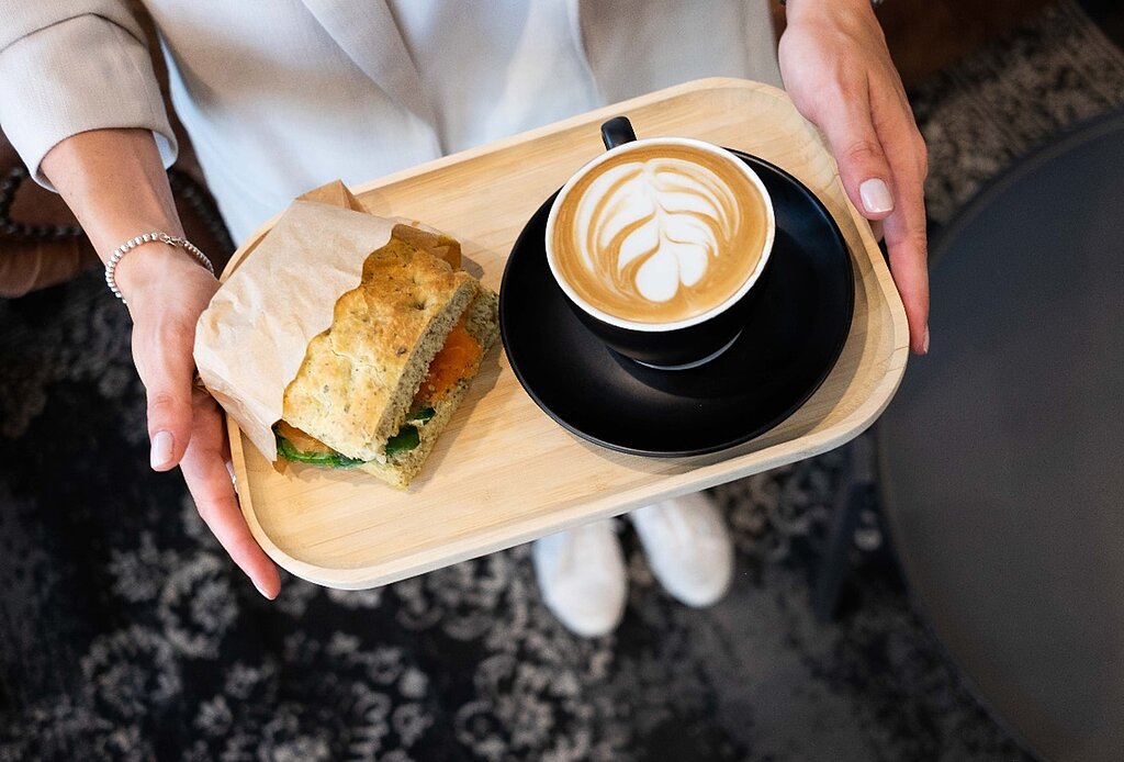 Ein Holztablett mit einem Cappuccino und einer Stulle mit Gemüse.