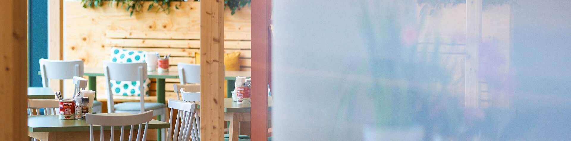 Tische und Sessel in einer Kantine. Die Sitzgelegenheiten sind aus Holz und schön dekoriert.