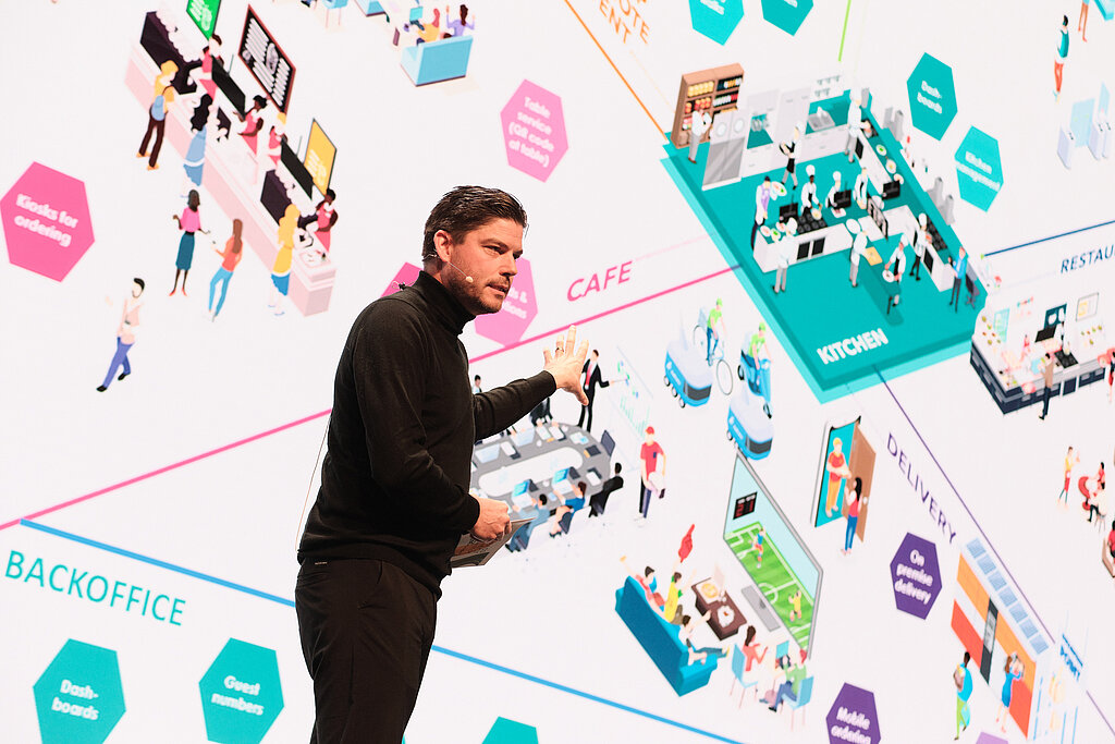Ein Vortragender, der vor einer Powerpointslide steht und mit der Hand auf die Slide zeigt. Auf der Slide ist ein Digitales Ökosystem zu sehen.