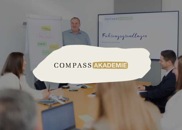 Ein Lehrender der vor einem Bildschirm und neben einem Flipchart steht. Davor das Logo der Compass Akademie.