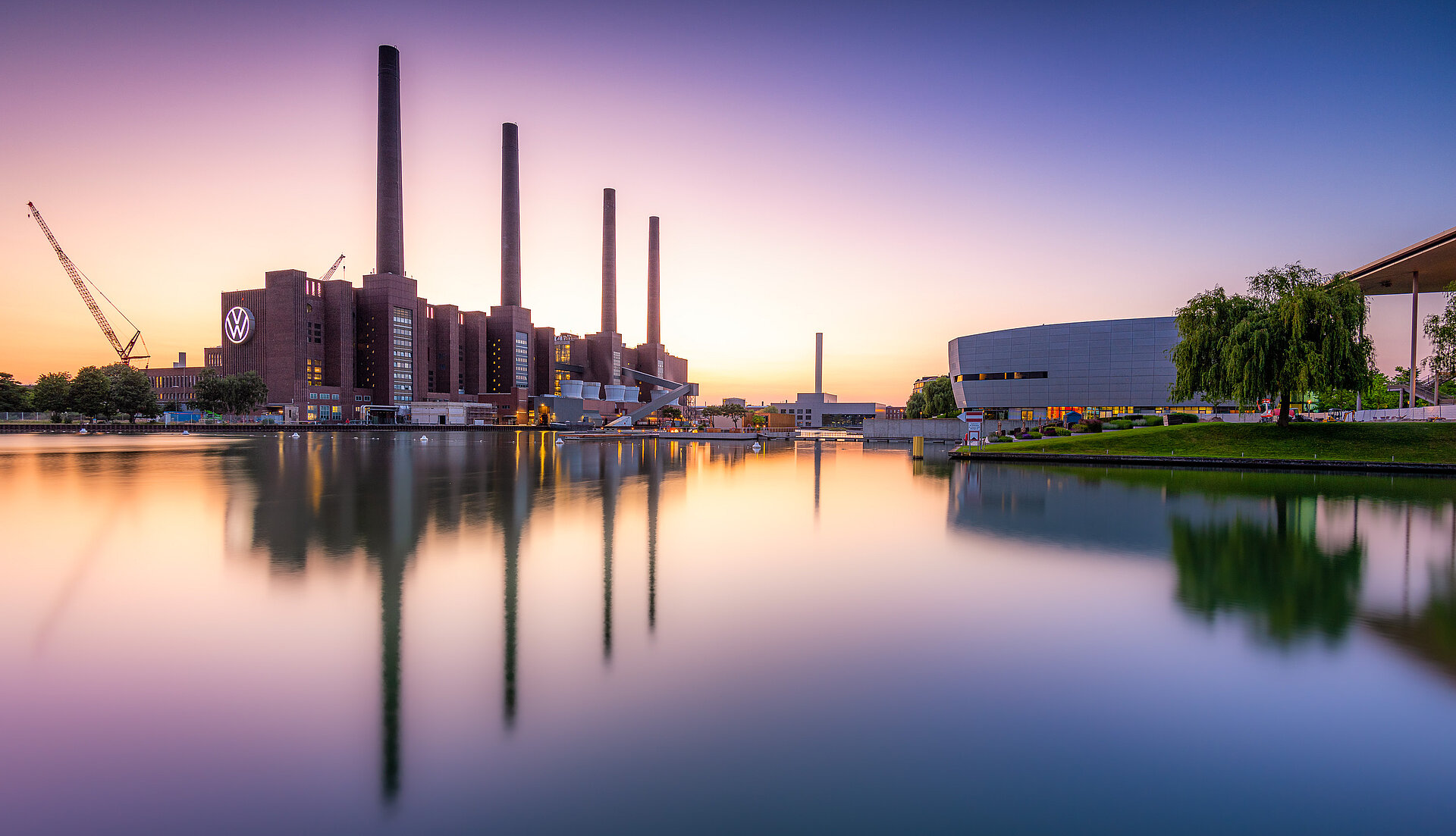 Das Volkswagenwerk, bzw. die Autostadt in Wolfsburg, fotografiert von einem Fluss aus. Der Himmel im Hintergrund ist lila-organe.