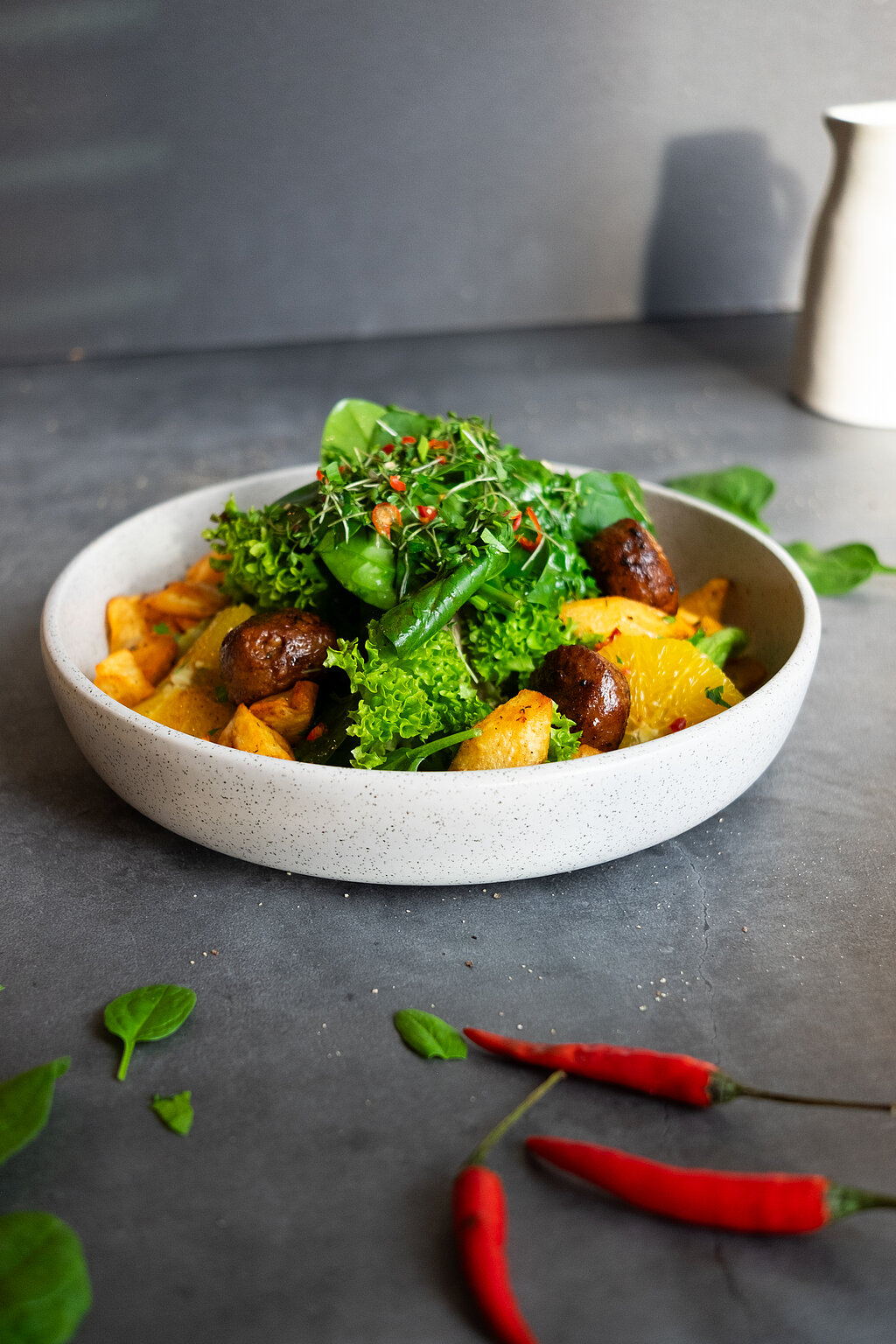 Ein veganes Gericht mit viel Gemüse und Blattspinat. Das Gericht ist schön angerichtet und davor liegen rote Chilischoten.