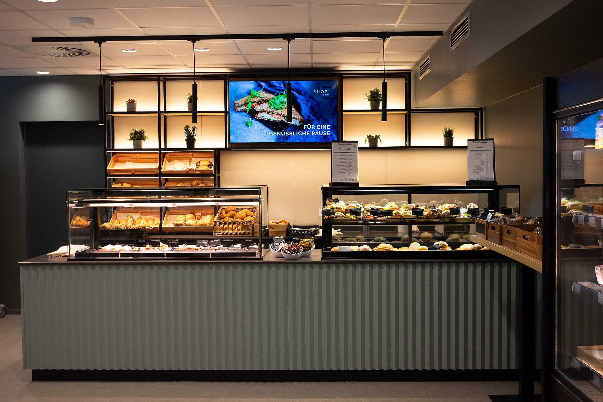 Eine Theke/Kaffeebar, die schön gestaltet und beleuchtet ist. Mittig ist ein Monitor mit einer Stulle platziert.