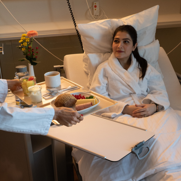 Healthcare & Senior Living Eine Patientin, die in einem Krankenbett liegt und gerade ihre Mittagsmahlzeit serviert bekommt.