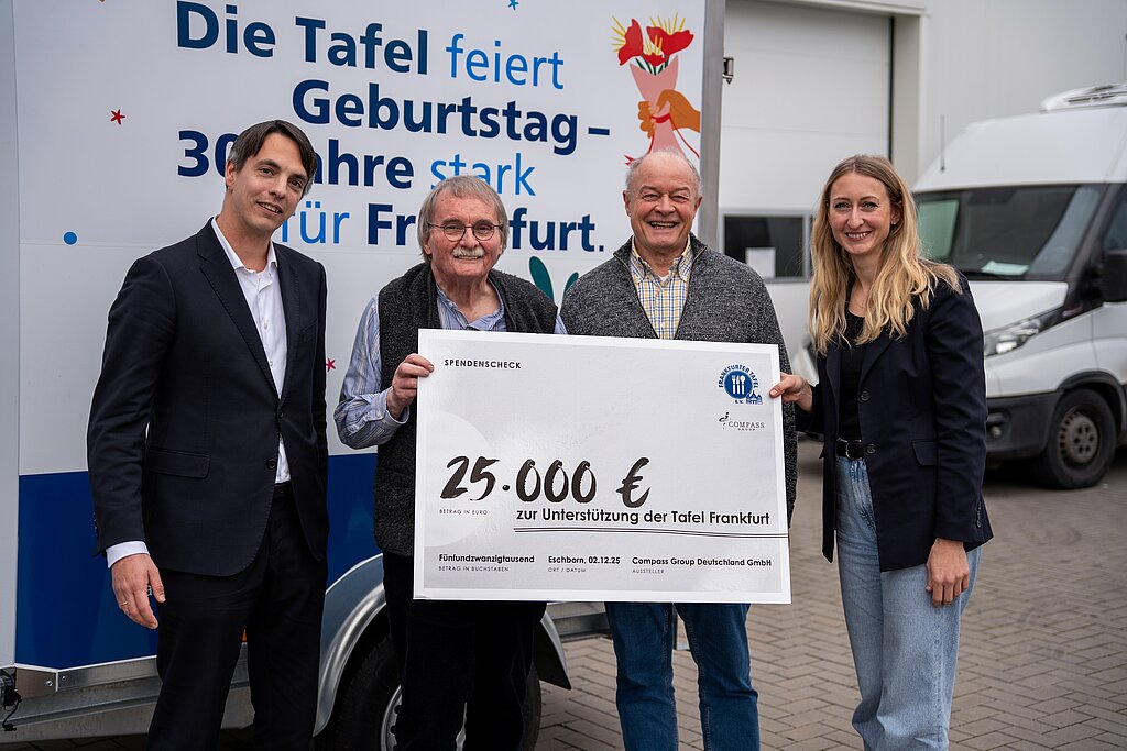Vier Personen, zwei von Compass Group Deutschland GmbH und zwei von der Tafel Frankfurt. Sie alle lachen freundlich in die Kamera. Der Tafel Frankfurt wurde ein Spendenscheck in der Höhe von 25.000 Euro von der Compass Group übergeben. 