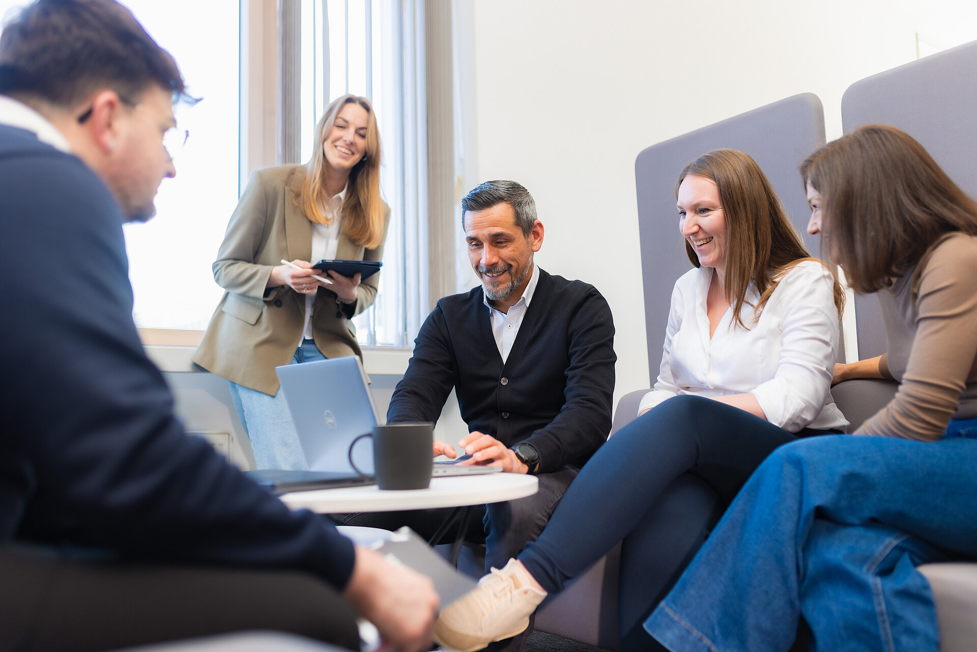 Ein Team von jungen Kolleginnen und Kollegen, das auf einer Couch um einen Tisch sitzt und in einen Laptop schaut und etwas bespricht.