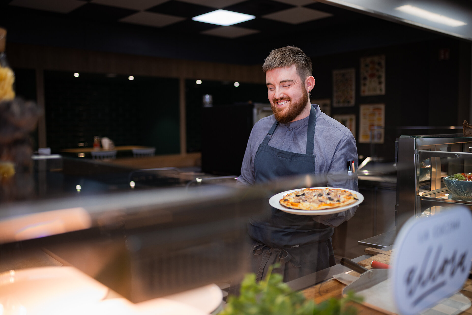 Ein junger Koch, der am Counter eine Pizza in der Hand hält.