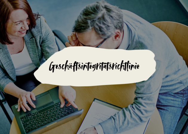 Zwei Personen, die an einem Tisch sitzen und in einen Laptop schauen.