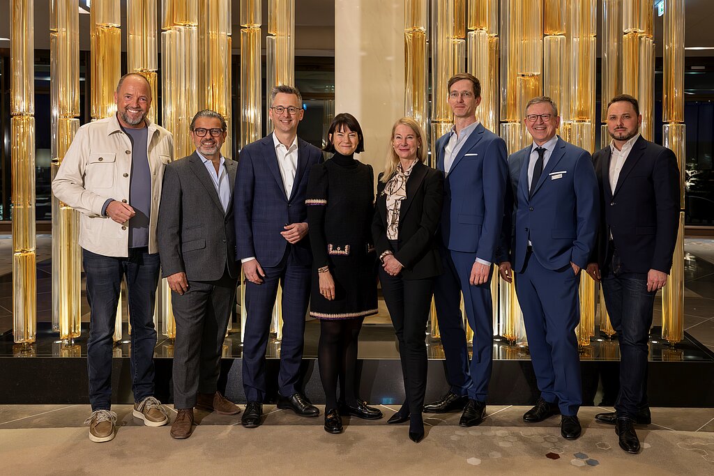 Ein Bild von Manager:innen in Businesskleidung - Anzügen und Kostümen - sie stehen in einer Lobby.