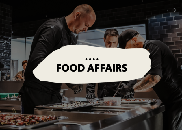 Food Affairs Drei Köche die in einer Küche hochwertige Speisen zubereiten.