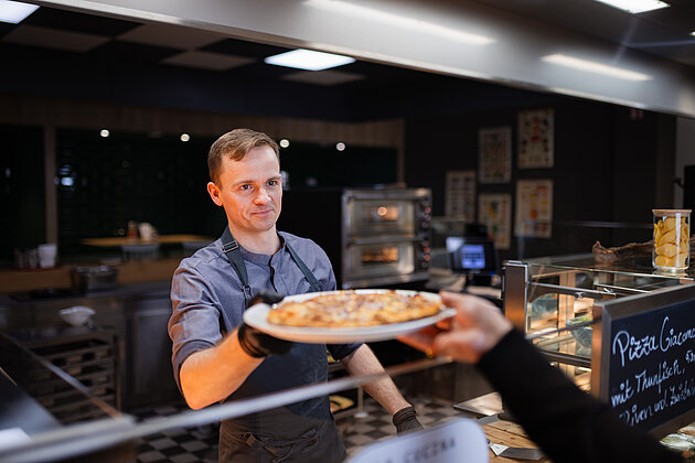 Business & Industry Ein junger Koch, der einem Gast eine Pizza über die Ausgabestelle gibt.
