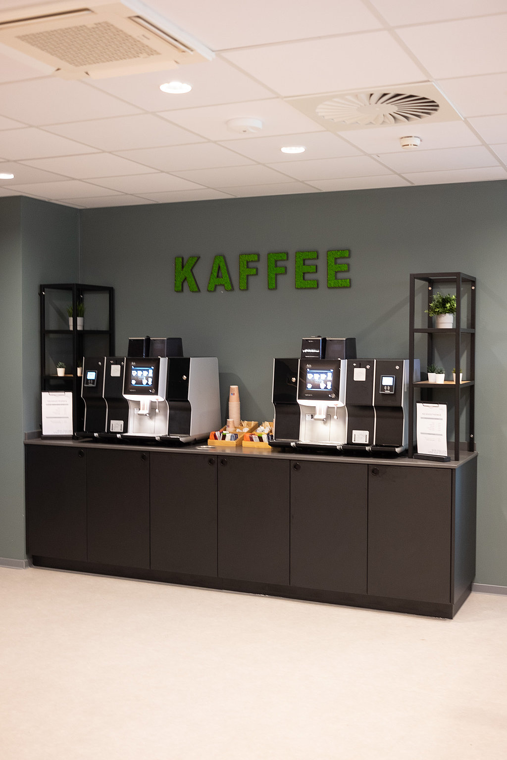 Eine Kaffeebar an einer blaugrünen Wand, darüber in grün der Schriftzug "Kaffee". 