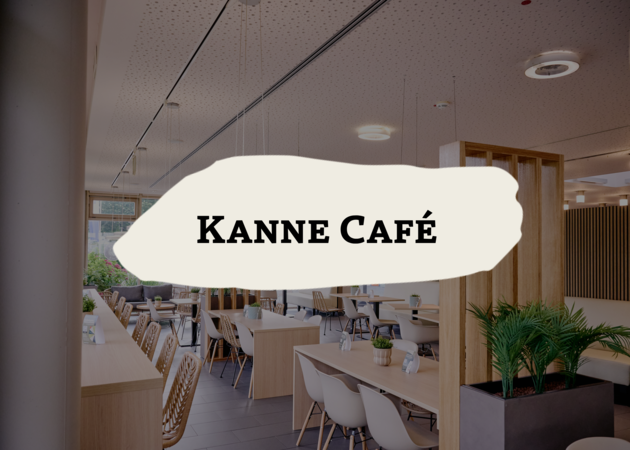 Ein gemütlich eingerichtetes Cafe, es sind helle Stühle und Tische mit hellem Holz zu sehen. Davor ist das Logo der Compass Group Retailbrand Kanne Cafe zu sehen.