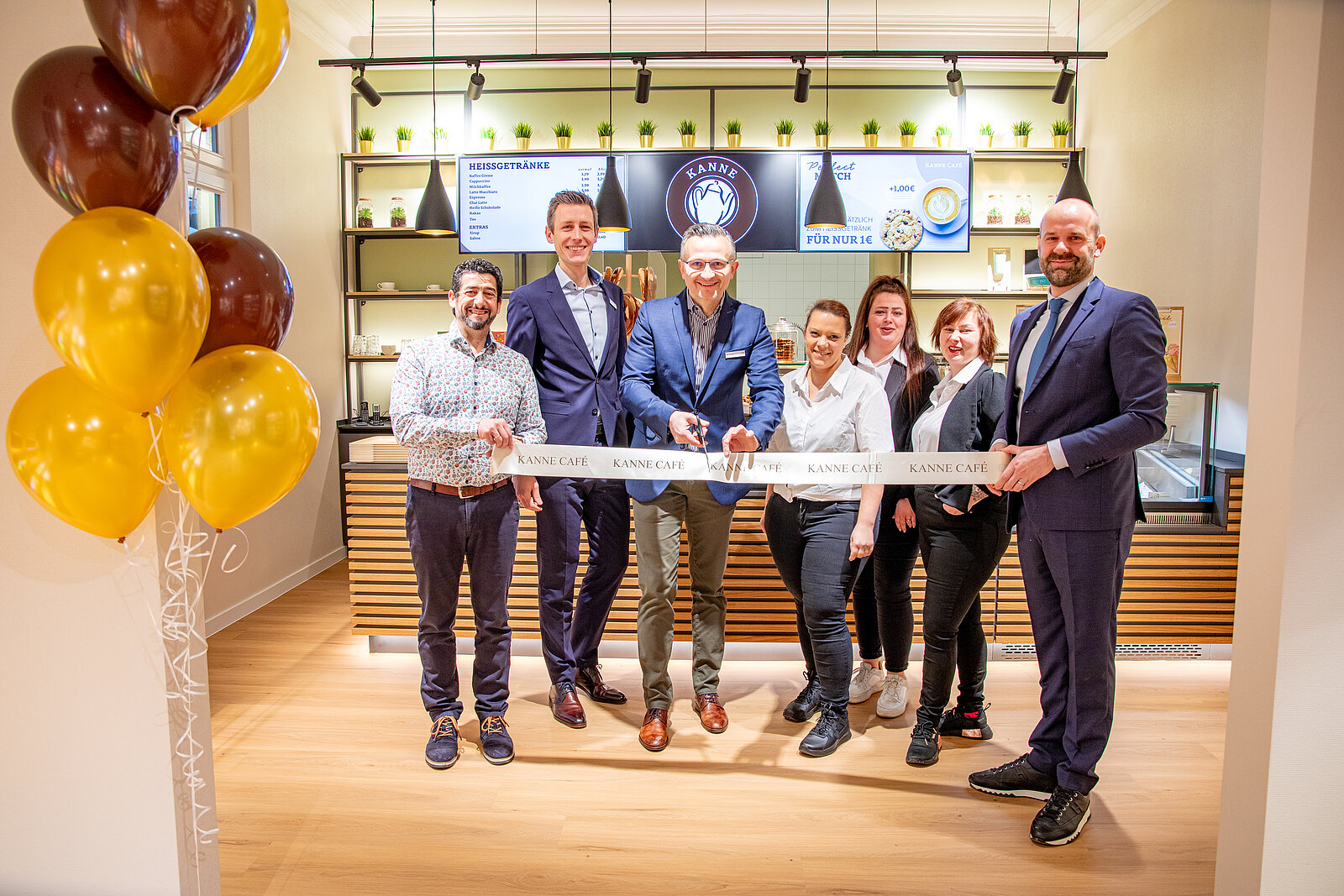 Das Team von Kanne Café in der Fachklinik Bad Benntheim gemeinsam mit der Klinikleitung bei der Eröffnung des Cafes. Die Personen stehen vor der Theke und schneiden ein Band durch.