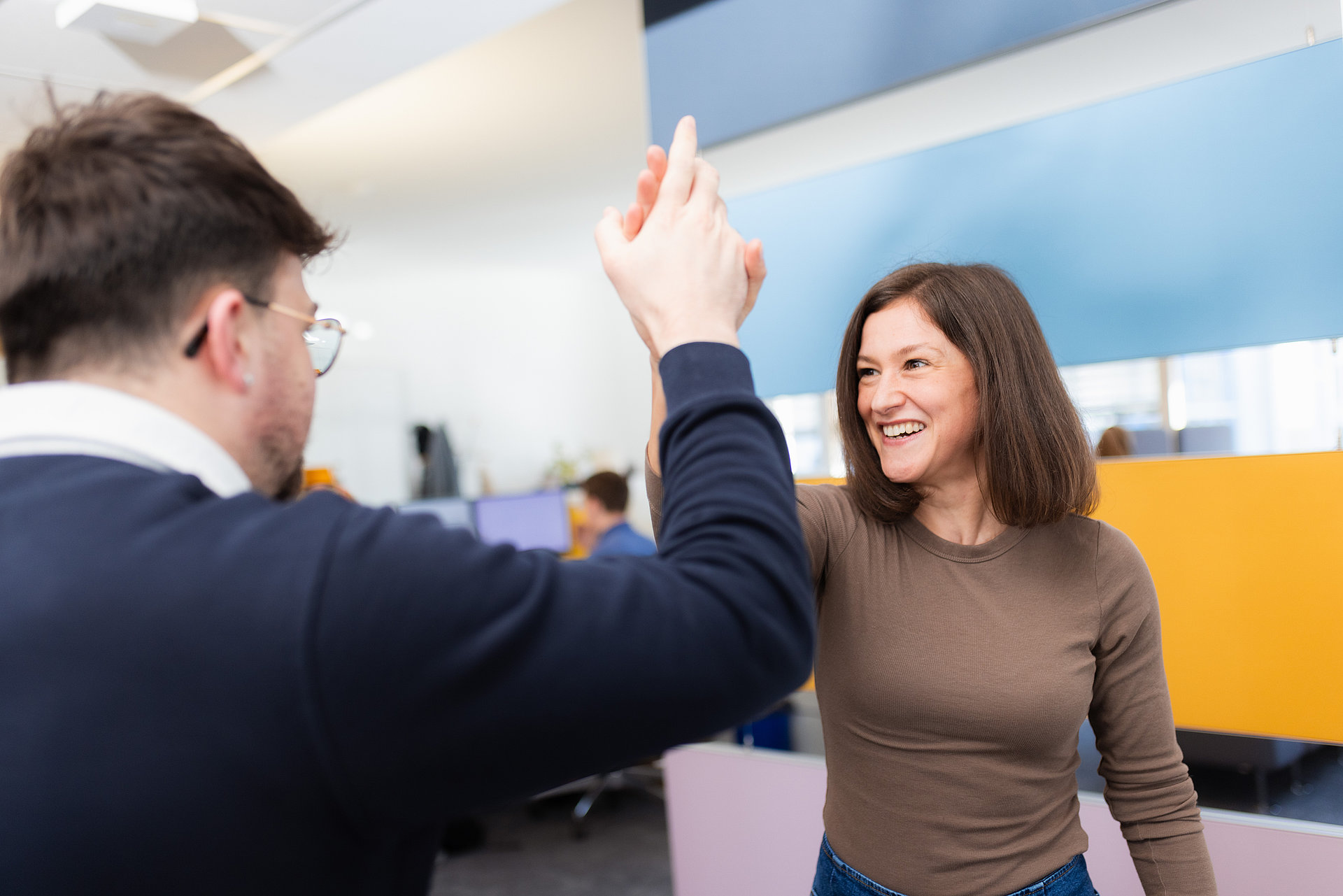 Eine junge Frau und ein Mann, die sich im Büro ein High five geben.