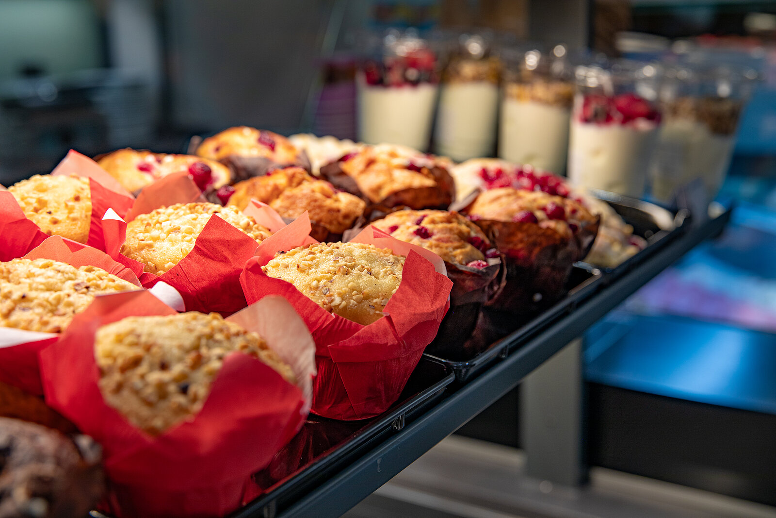 Muffins und Joghurt mit Beeren und Müsli in einer Vitrine.